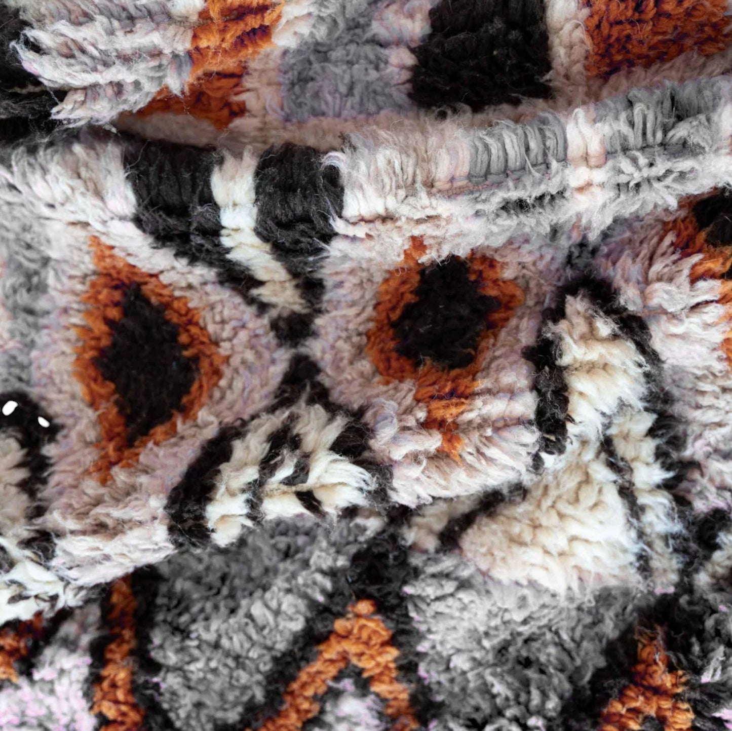 A handmade Moroccan wool rug featuring a sophisticated geometric diamond pattern in neutral tones, orange, and black, accented with intricate details and tassels on the edges. This rug blends traditional Berber craftsmanship with modern interior design styles.