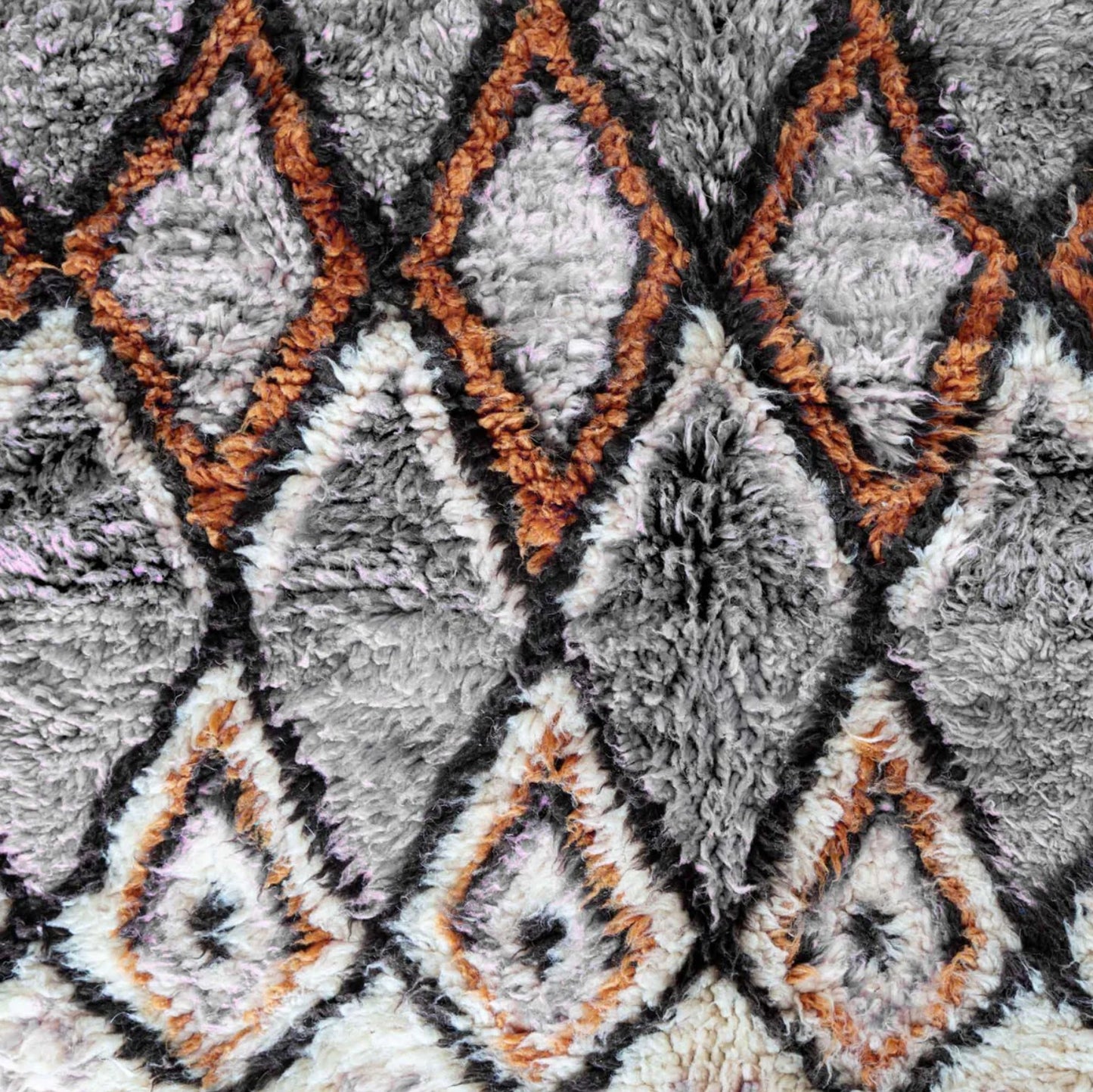 A handmade Moroccan wool rug featuring a sophisticated geometric diamond pattern in neutral tones, orange, and black, accented with intricate details and tassels on the edges. This rug blends traditional Berber craftsmanship with modern interior design styles.