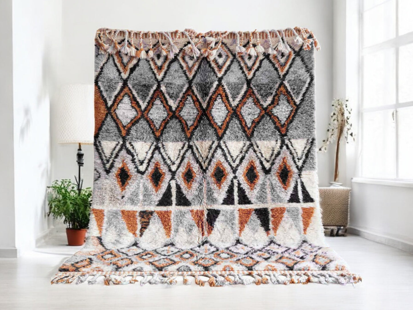 A handmade Moroccan wool rug featuring a sophisticated geometric diamond pattern in neutral tones, orange, and black, accented with intricate details and tassels on the edges. This rug blends traditional Berber craftsmanship with modern interior design styles.