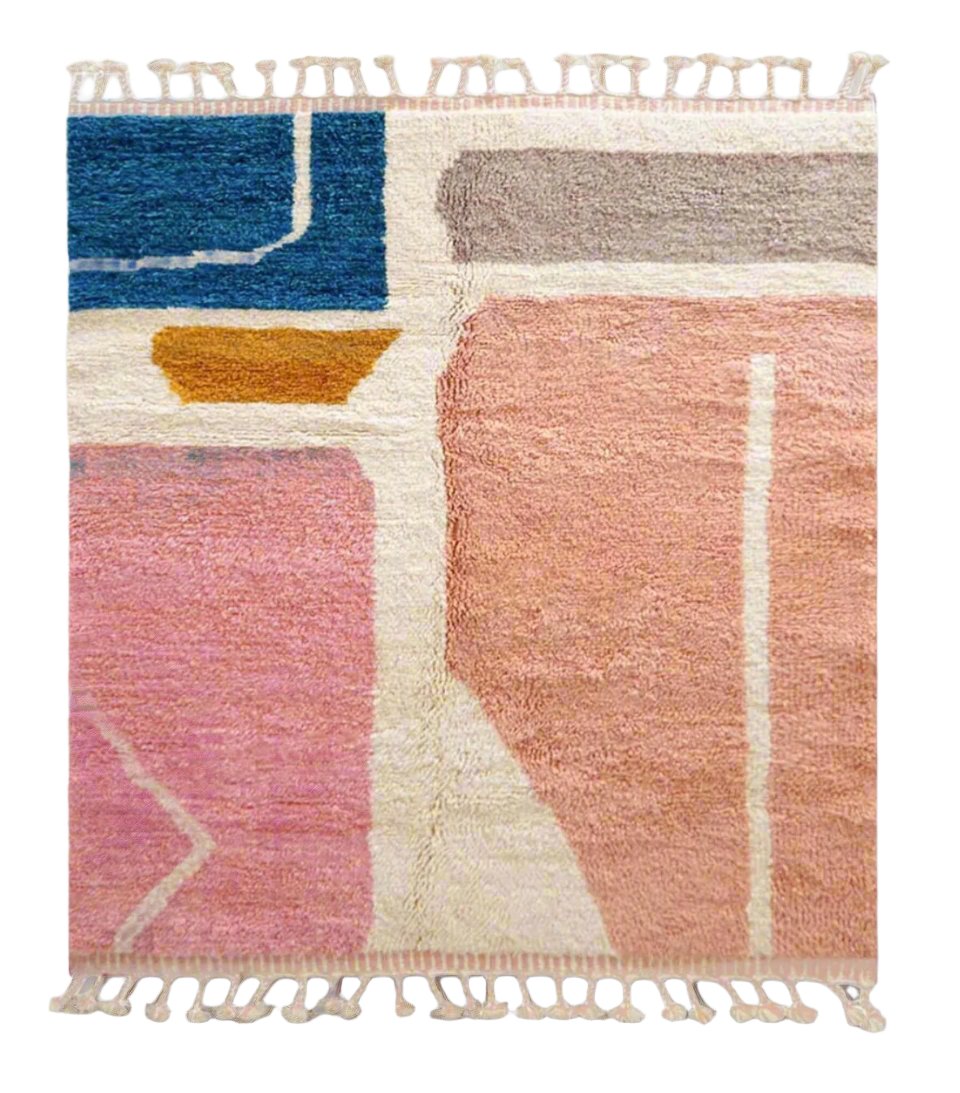 A handmade Moroccan wool rug featuring a vibrant color block design with shades of pink, blue, mustard yellow, and neutral tones, accented by tassels along the edge. Displayed against a bright yellow wall with natural green and wooden decor elements.