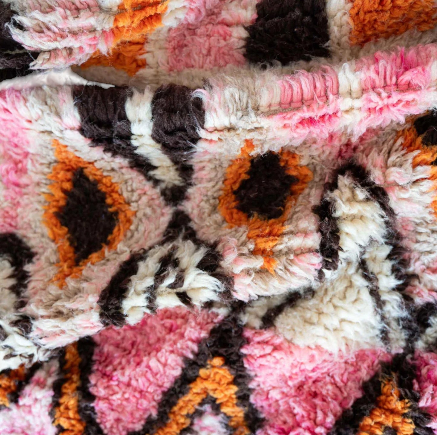 A handmade Moroccan wool rug featuring a vibrant geometric diamond pattern in shades of pink, orange, and black, with intricate detailing and tassels on the edges. A perfect blend of traditional Berber artistry and modern design aesthetics.