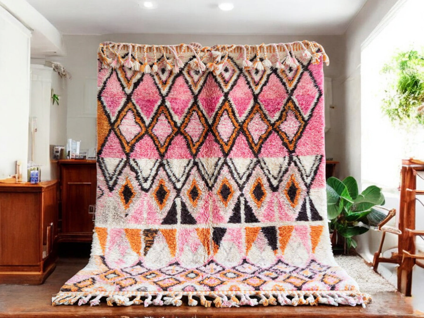 A handmade Moroccan wool rug featuring a vibrant geometric diamond pattern in shades of pink, orange, and black, with intricate detailing and tassels on the edges. A perfect blend of traditional Berber artistry and modern design aesthetics.