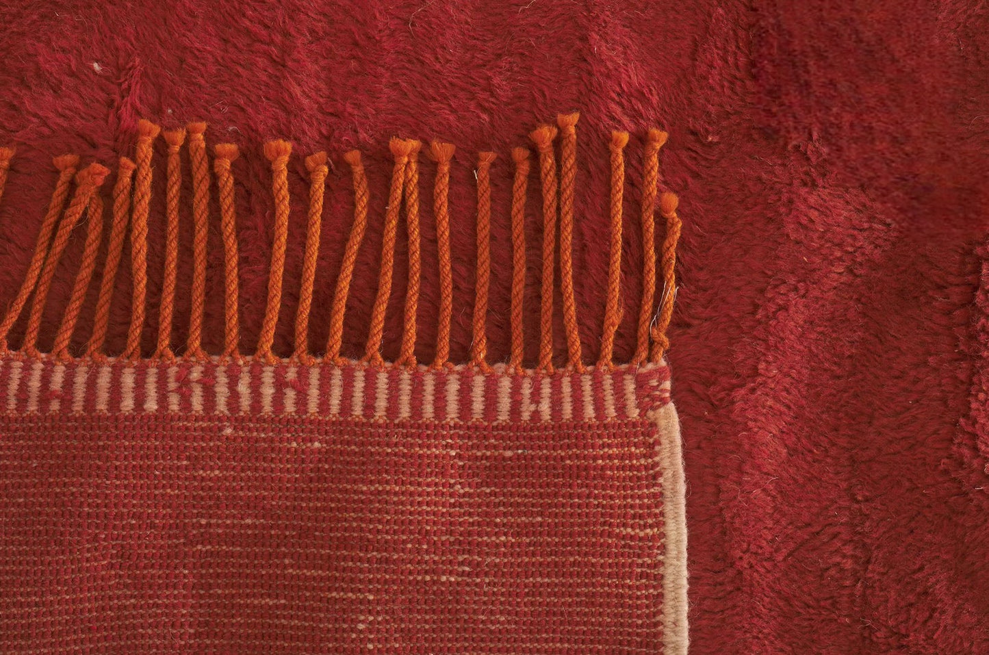 A minimalist Moroccan rug in deep red with subtle cream accents and tassel fringes on the edge. This natural wool rug adds warmth and style to any room and is customizable to fit various spaces.
