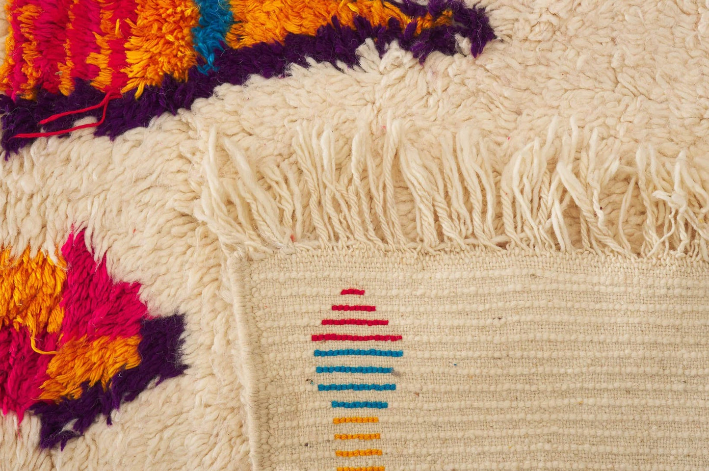 A vibrant Moroccan Boucherouite rug with a bold, colorful abstract pattern on a cream background. Made from natural wool, this rug adds energy and character to bohemian and eclectic interiors and is available in custom sizes.