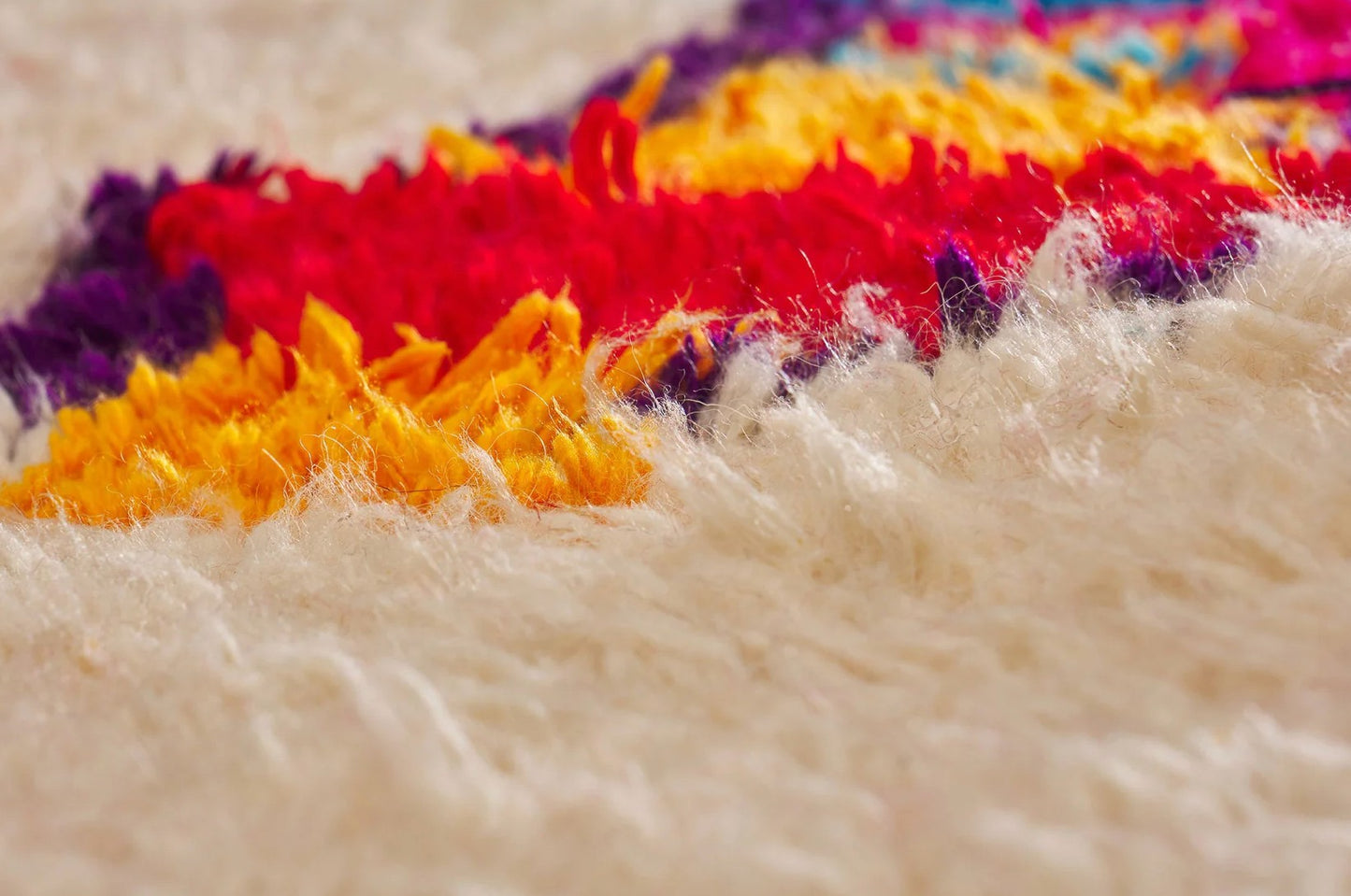 A vibrant Moroccan Boucherouite rug with a bold, colorful abstract pattern on a cream background. Made from natural wool, this rug adds energy and character to bohemian and eclectic interiors and is available in custom sizes.