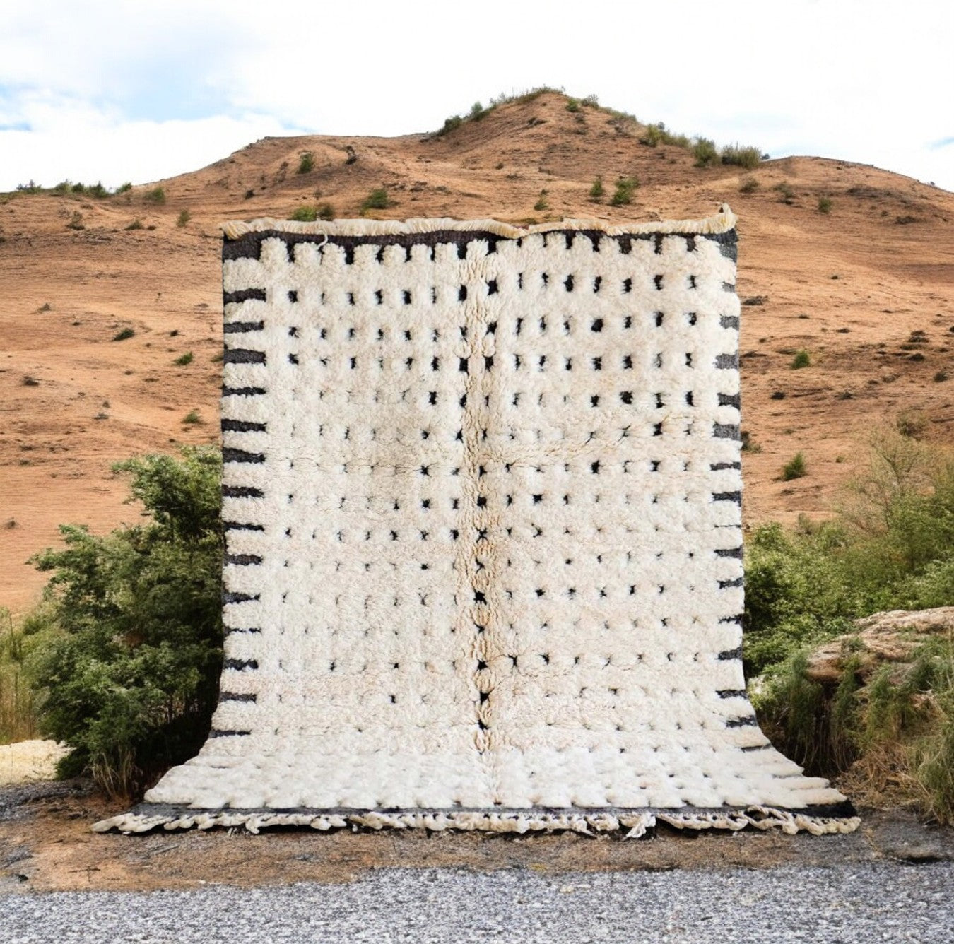 Artisanal handmade wool rug in white with a dotted black stripe pattern and delicate fringed edges, displayed on a warm wooden floor, ideal for minimalist and modern decor.