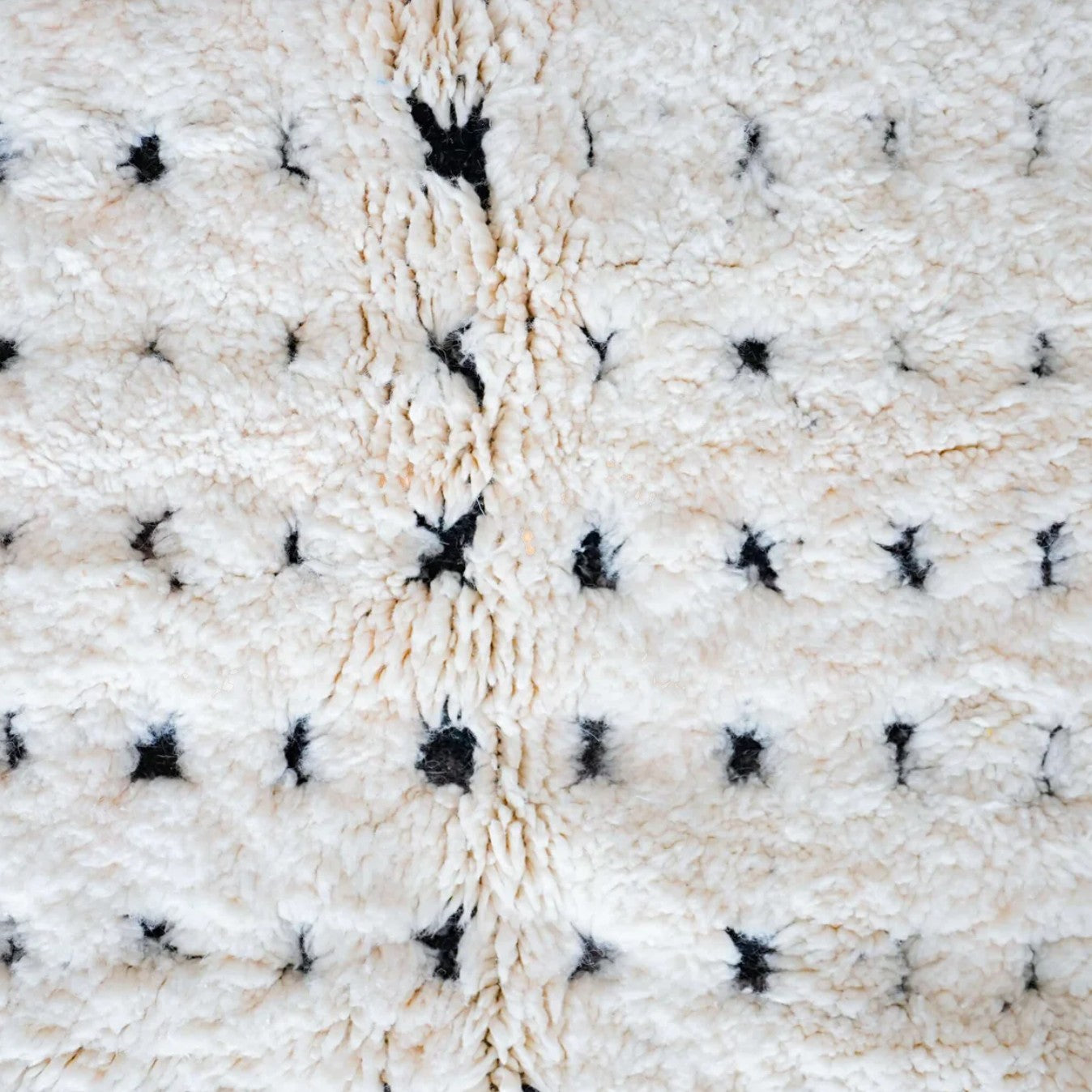 Artisanal handmade wool rug in white with a dotted black stripe pattern and delicate fringed edges, displayed on a warm wooden floor, ideal for minimalist and modern decor.