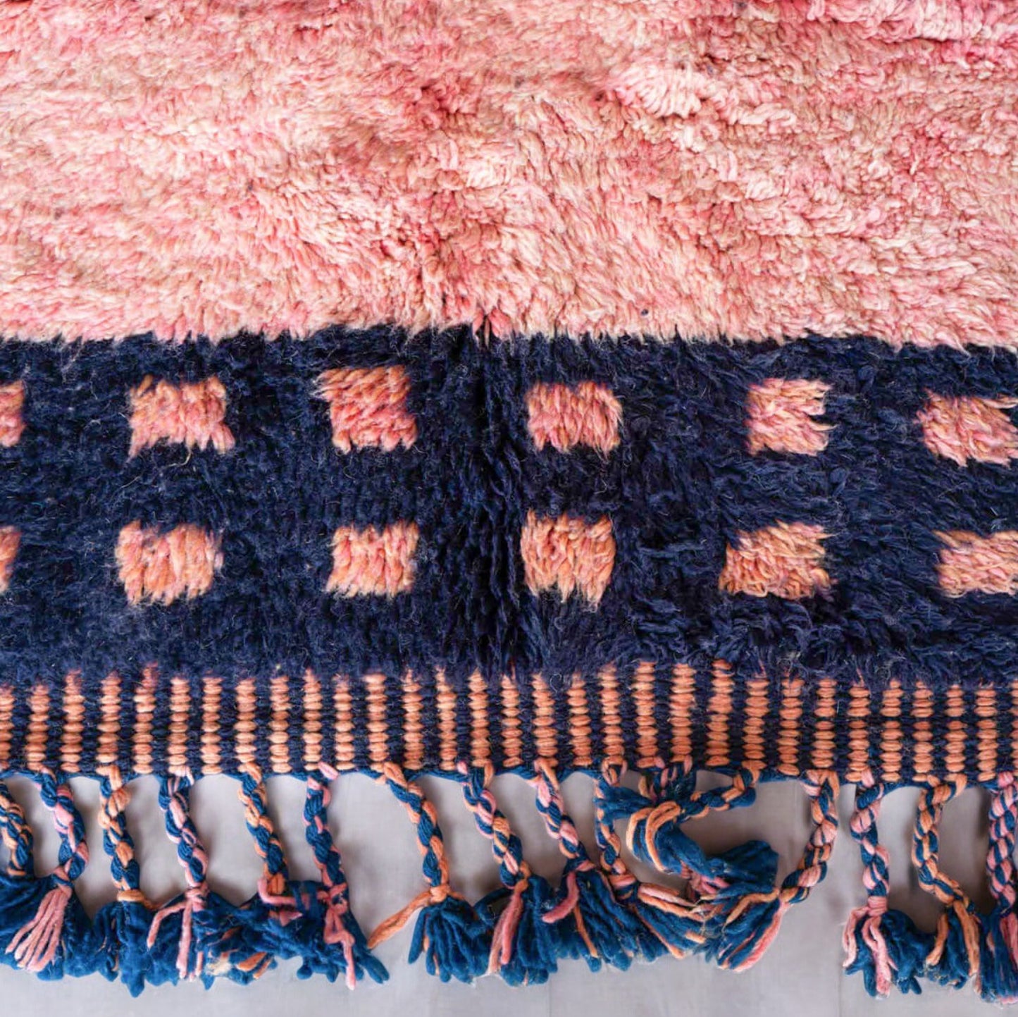 Handmade Moroccan wool rug featuring a vibrant pink center with a navy checkered border and fringed edges, creating a bold and stylish look for modern, boho, or eclectic interiors