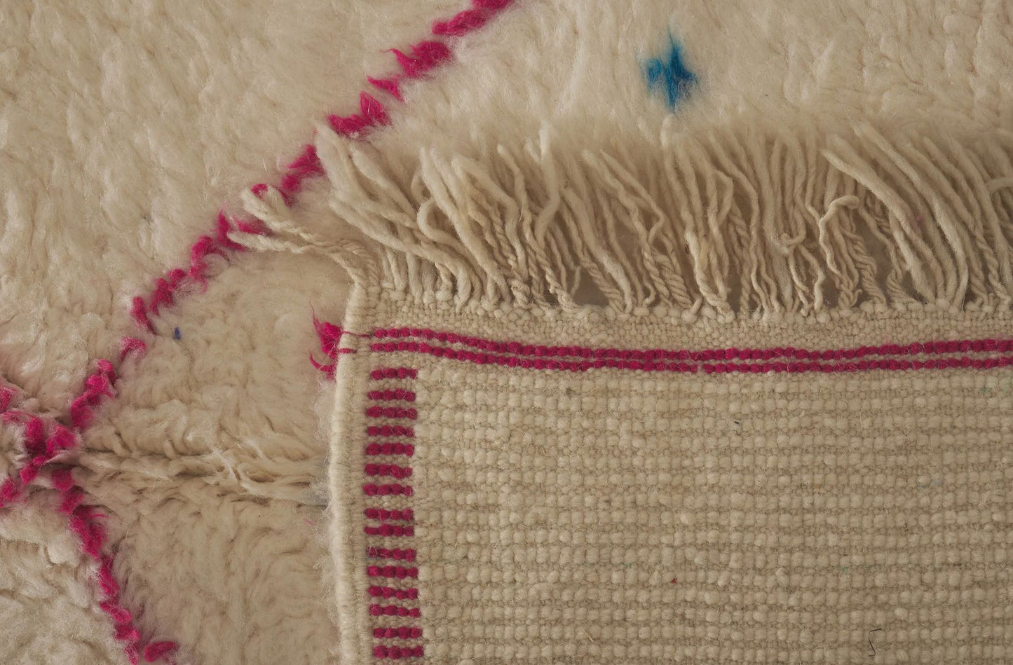 Ivory Moroccan rug with pink diamond pattern and blue accents, featuring a bold blue bar across the design. This handmade rug adds a colorful boho touch to living rooms, bedrooms, or office spaces.