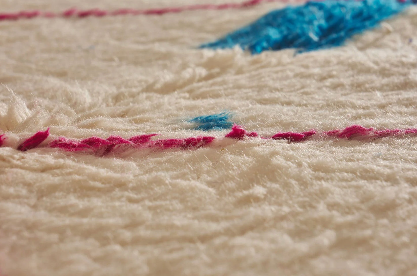 Ivory Moroccan rug with pink diamond pattern and blue accents, featuring a bold blue bar across the design. This handmade rug adds a colorful boho touch to living rooms, bedrooms, or office spaces.