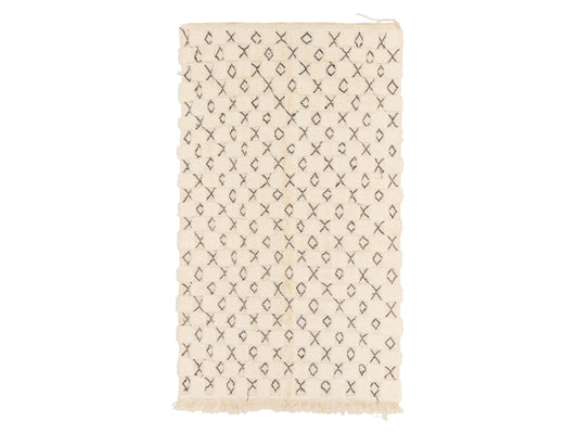 A Moroccan shag rug in cream with a black diamond and cross pattern, crafted from natural wool. This rug features a unique design with tassel fringes and is customizable to any size, adding warmth and style to modern or traditional interiors.
