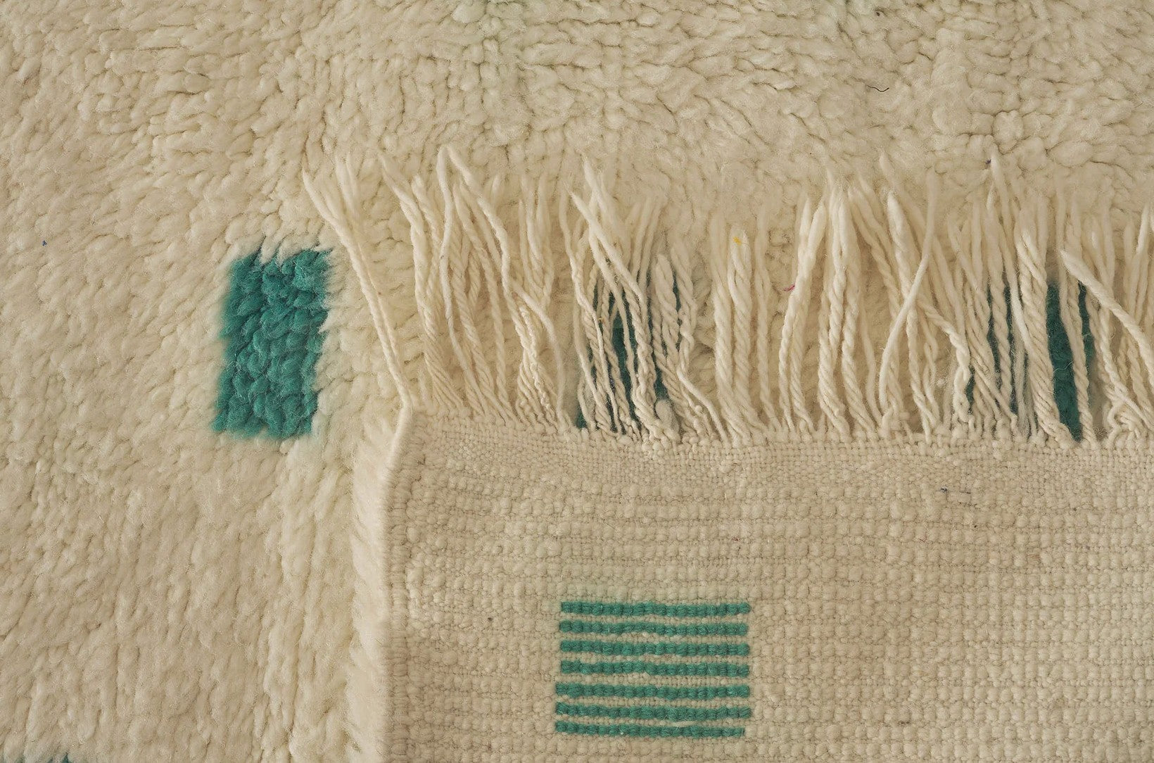 A contemporary Moroccan rug with turquoise geometric patterns on a cream wool base, handwoven for a modern minimalist style. Ideal for living rooms, bedrooms, or offices, this rug is available in customizable sizes.
