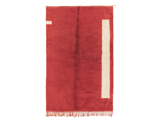 A minimalist Moroccan rug in deep red with subtle cream accents and tassel fringes on the edge. This natural wool rug adds warmth and style to any room and is customizable to fit various spaces.
