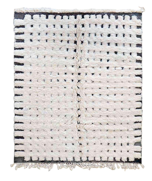 Artisanal handmade wool rug in white with a dotted black stripe pattern and delicate fringed edges, displayed on a warm wooden floor, ideal for minimalist and modern decor.