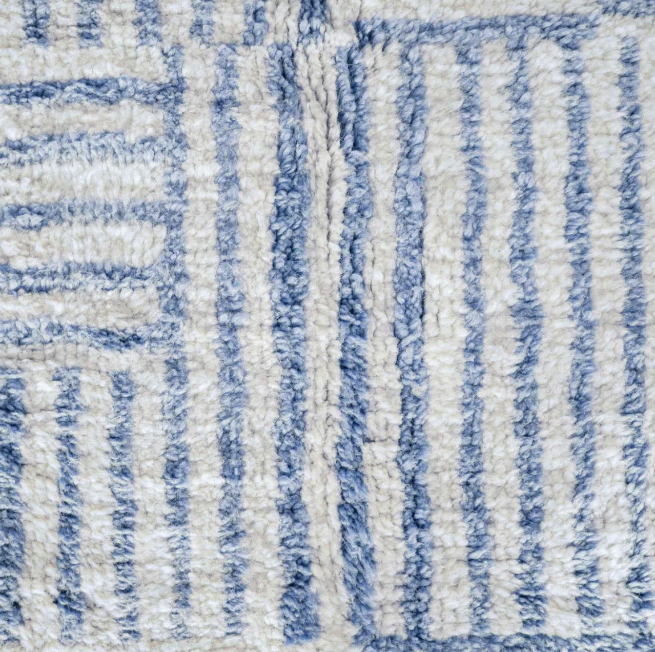 Artisanal handmade wool rug in a sky blue and white striped patchwork design, accented by delicate fringe, displayed on a natural wooden floor, ideal for coastal and modern decor.