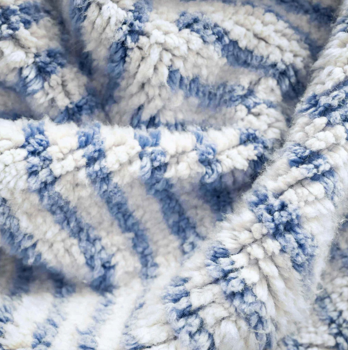 Artisanal handmade wool rug in a sky blue and white striped patchwork design, accented by delicate fringe, displayed on a natural wooden floor, ideal for coastal and modern decor.