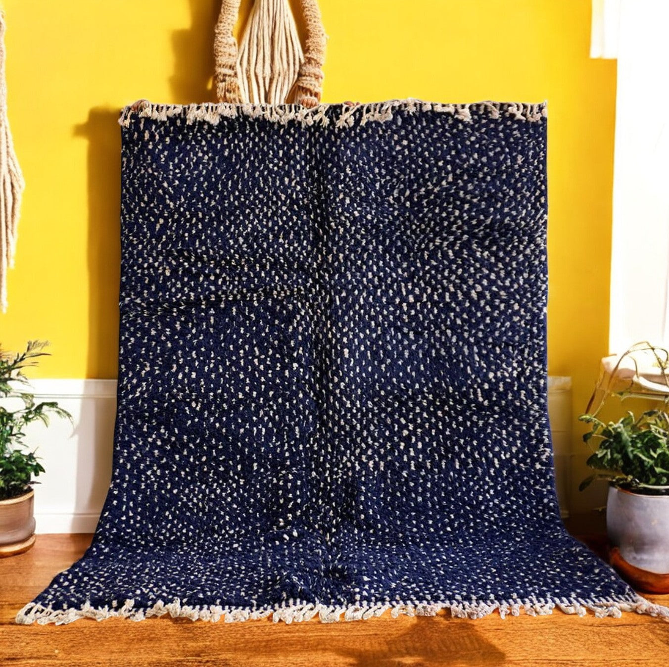 Handmade wool rug in a rich deep blue color, featuring a delicate dotted pattern and subtle fringed edges, displayed on a textured concrete background for a sophisticated look.