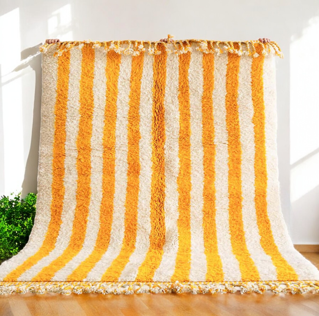 Artisanal handmade wool rug featuring bold yellow and white vertical stripes, accented by intricate fringe detailing, displayed on a neutral gray background, ideal for bright and cheerful modern decor.