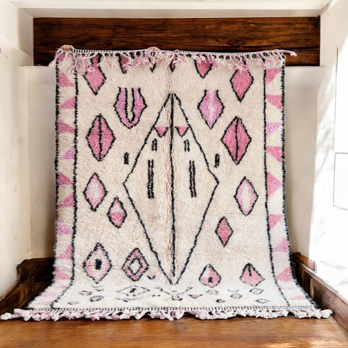 Handmade wool rug in soft white featuring pastel pink and black tribal geometric patterns, adorned with intricate fringe detailing, ideal for bohemian and modern feminine decor styles.