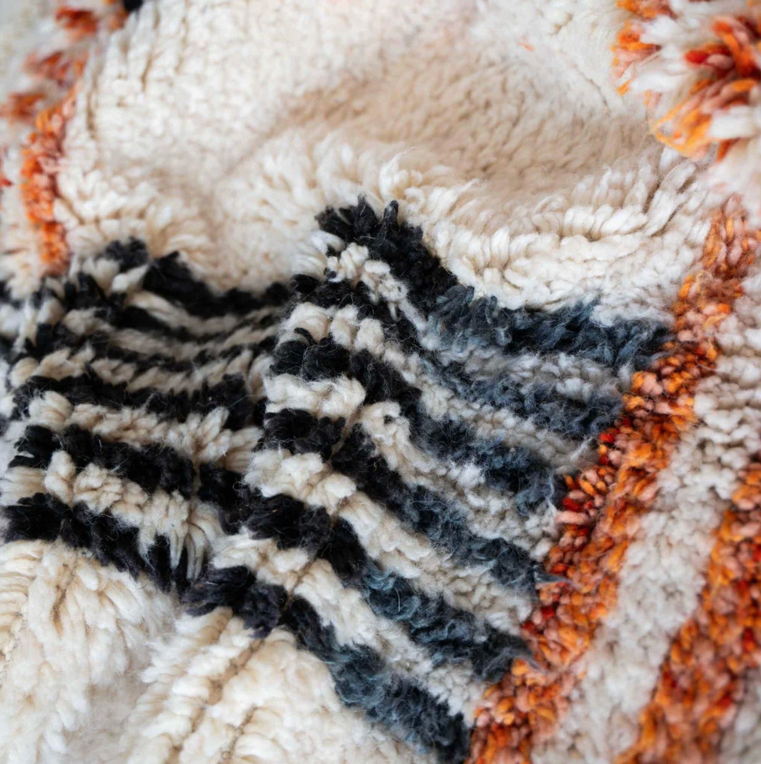 Artisanal handmade wool rug with vibrant orange and black geometric cross patterns on a soft white base, accented by intricate fringed edges, ideal for modern and eclectic decor.