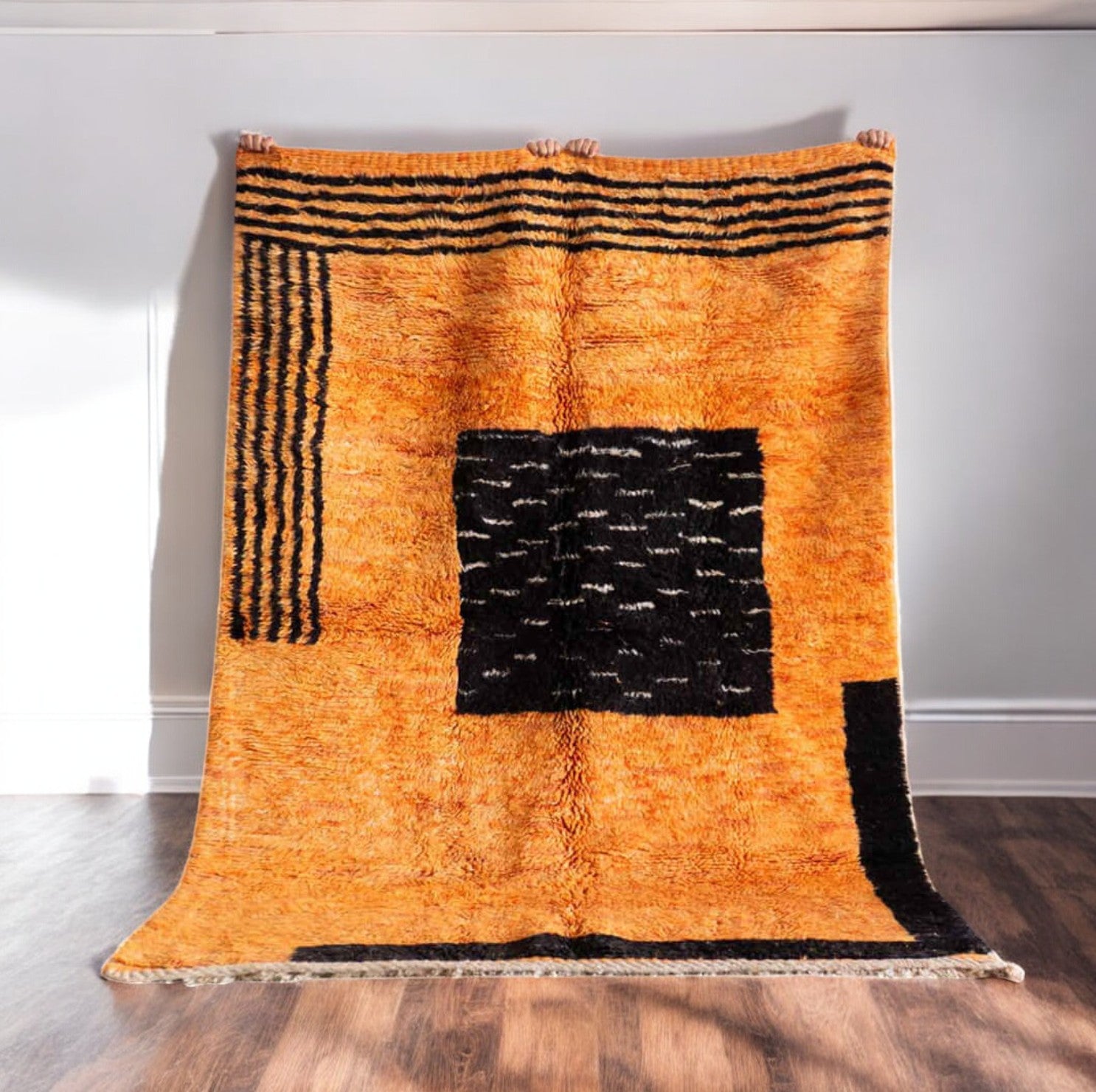 Handmade wool rug with bold black abstract shapes and linear patterns on a vibrant orange background, crafted with intricate texture and detailing, ideal for statement modern or eclectic decor.