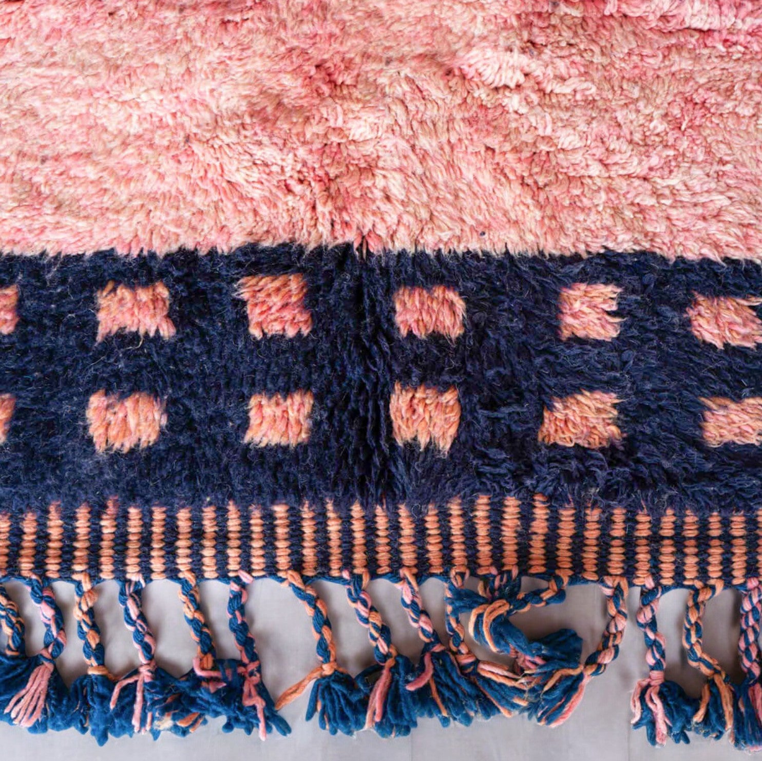 Handmade Moroccan wool rug featuring a vibrant pink center with a navy checkered border and fringed edges, creating a bold and stylish look for modern, boho, or eclectic interiors
