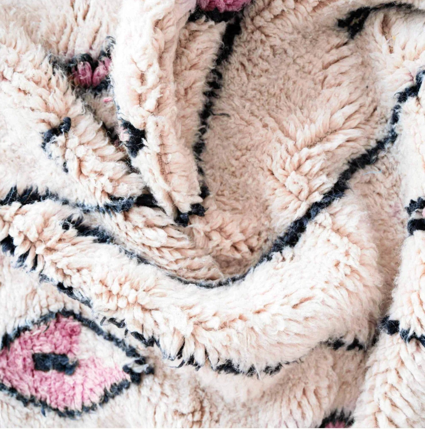 Handmade Moroccan wool rug with a cream base featuring pink geometric patterns and black outlines, finished with fringed edges, ideal for minimalist, boho, or Scandinavian interiors

