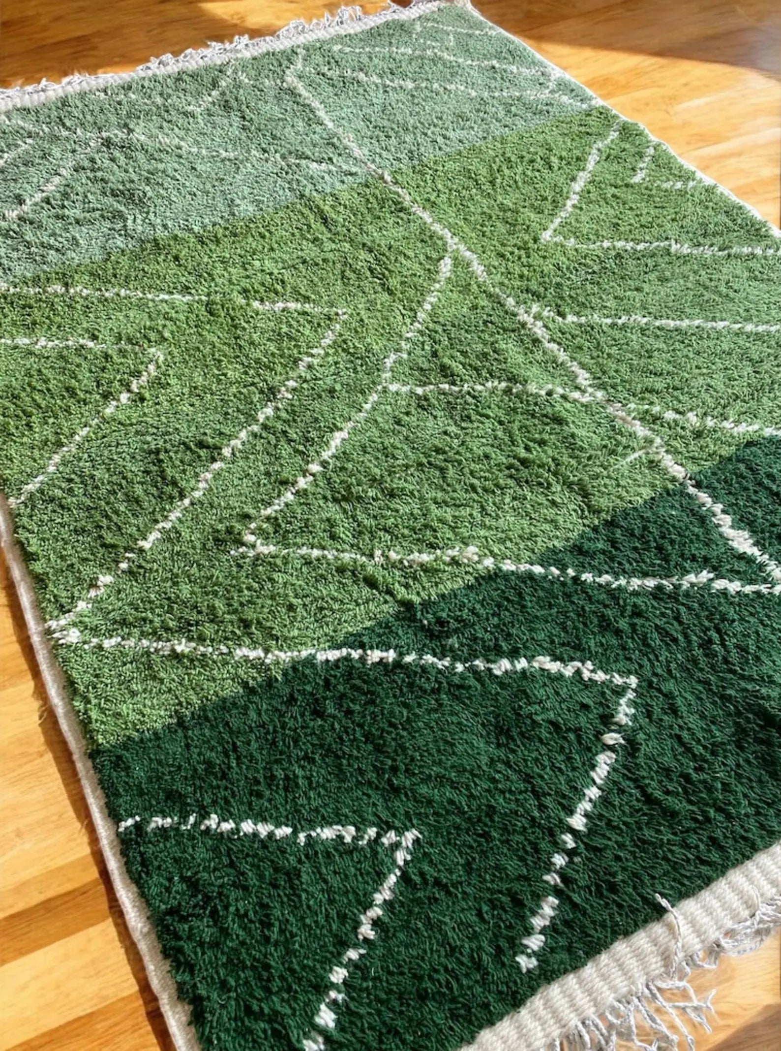 Handmade Moroccan rug in rich green shades with white diamond geometric lines. This Berber wool carpet is woven by skilled artisans using traditional Moroccan techniques, making each rug unique. Its fresh green tones bring life, balance, and a calming natural touch to interiors. Perfect for living rooms, bedrooms, and creative spaces, this eco-friendly wool rug blends tribal heritage with modern bohemian style for timeless Moroccan elegance.