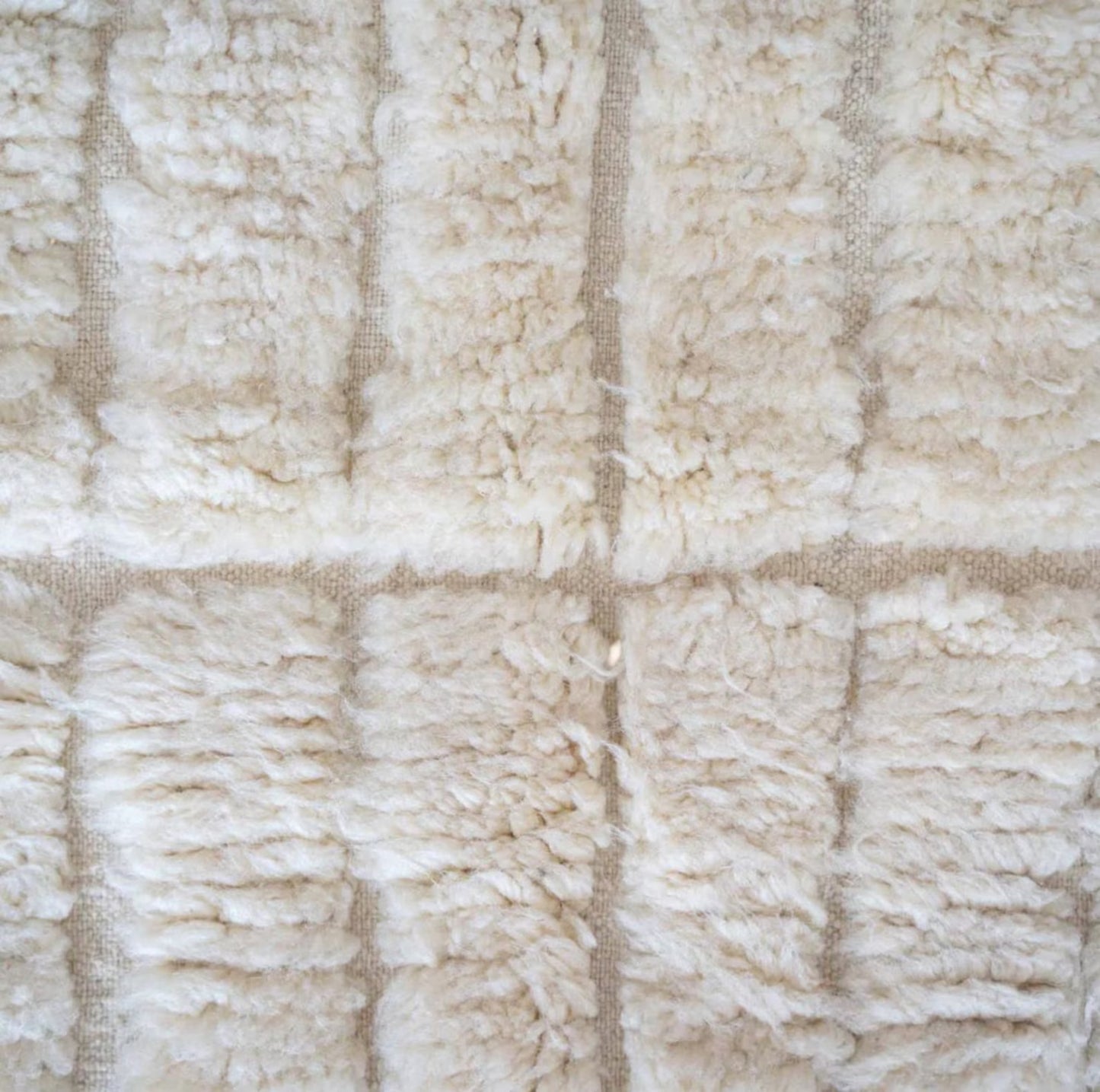 This handmade Moroccan rug features a luxurious cream white wool texture with a minimalist grid pattern. Ethically handwoven by Berber women in the High Atlas Mountains, it brings softness, warmth, and authenticity to any living room, bedroom, or serene corner. Perfect for Japandi, boho, minimalist, or modern interiors. Crafted from 100% natural wool with exquisite care. Custom sizing available for your space.